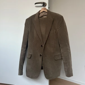 Brun manchesterkostym Acne Studios - Säljer en snygg brun manchesterkostym från Acne Studios. Kavajen har klassisk passform med två knappar och fickor med lock. Byxorna är raka och matchar perfekt. Kostymen är i mjuk manchester och har en stilren, tidlös look. Byxorna är i 52, osäker på kavajens storlek, men den är runt L.