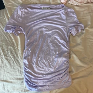 Ljuslila topp från AWARE, storlek M - Supersöt ljuslila topp från AWARE med korta ärmar och boatneck-ringning. Tillverkad i ett mjukt och lätt material som känns skönt mot huden. Perfekt att styla med jeans eller kjol för en fräsch look. Säljes med originaltaggar kvar!