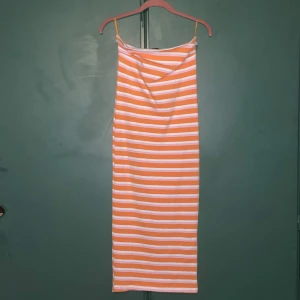 Randig fodralklänning från Gina Tricot - Säljer en lång, off shoulder fodralklänning från Gina Tricot. Klänningen har horisontella ränder i orange, rosa och vitt. Den är figurnära och har en enkel, stilren design som känns perfekt för varma dagar. Använd 1 gång