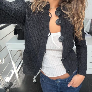 Svart stickad kofta med stora knappar - Snygg svart stickad kofta med stora, iögonfallande knappar framtill och två fickor. Perfekt att slänga över en topp för en chill men ändå uppklädd look.