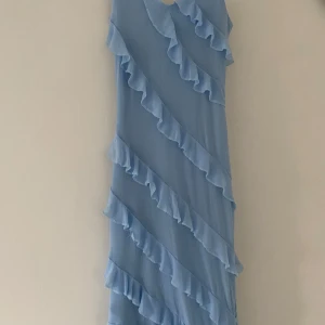 Ljusblå volangklänning med mesh - Supersöt ljusblå klänning med volanger i flera lager och mesh-tyg. Klänningen har en luftig känsla och är perfekt för sommarens alla tillfällen. Den har en rak passform och volangerna ger en lekfull vibe.