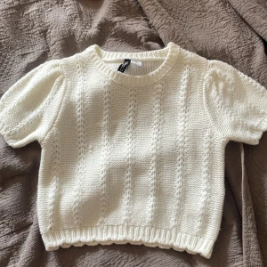 Vit stickad tröja från Gina Tricot XS - Supersöt vit stickad tröja från Gina Tricot i storlek XS. Tröjan har korta puffärmar, rund halsringning och ett snyggt stickat mönster med ribbade kanter. Perfekt för lager-på-lager och ger en fräsch look till din outfit.