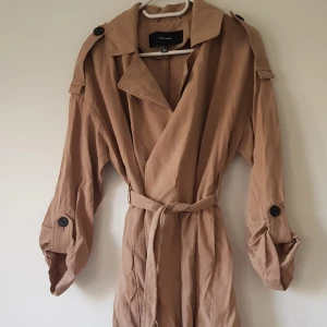 Beige trenchcoat från Vero Moda strl S - Snygg beige trenchcoat från Vero Moda med klassisk krage, knytskärp i midjan och knappar på axlar och ärmar. Jackan har en loose fit och är perfekt för vår och höst. Tillverkad i mjukt bomullsmaterial för en chill och stilren look.  Helt & fint skick