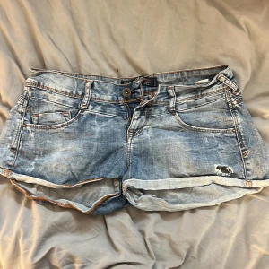 Blå jeansshorts med upprullad kant - Snygga lågmidjade blå jeansshorts med upprullad kant och slitna detaljer. Perfekta för varma dagar och ger en avslappnad vibe.