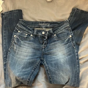 Blå jeans med broderad bakficka  - Snygga blå jeans från Luxury med markerade sömmar och en unik broderad bakficka med silverdetaljer och nitar. De är lågmidjade. Perfekta för dig som vill sticka ut med coola detaljer och en trendig look.