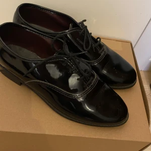 Lackskor!  - Snygga svarta skor i lackat skinn med klassisk snörning och låg klack. Skorna har rund tå och stilren design som passar perfekt till både dressade och avslappnade outfits. Perfekta för dig som gillar en tidlös och clean look. Endast använda 1 gång. Ge gärna prisförslag. Flera bilder finns! Hör av dig vid intresse! Gateway Formal Foot Wear