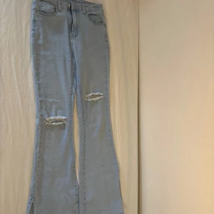 Ljusblå bootcut jeans med slits - Säljer ett par ljusblå jeans med bootcut och slits nertill. Byxorna har slitna detaljer vid knäna och klassisk femficksdesign. Perfekta för dig som gillar en avslappnad Stockholm och trendig look.