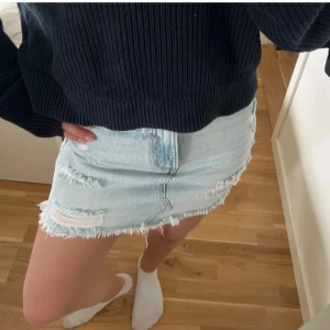 Ljusblå jeanskjol med slitningar - Trendig ljusblå jeanskjol från Bik Bok med rå kant och slitna detaljer framtill. Klassisk femficksmodell med knapp och dragkedja. Perfekt för dig som gillar en edgy och avslappnad stil.