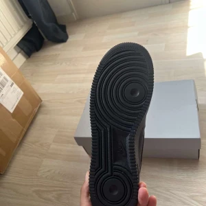 Nike Air Force 1 helsvarta sneakers - Klassiska Nike Air Force 1 i helsvart skinn med svart sula och svarta skosnören. Använd 3 gånger vid begravning…