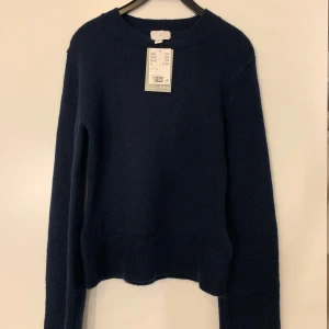 Mörkblå stickad tröja från H&M - Säljer nu min stickade tröja från H&M då den aldrig kommer till användning. Tröjan sitter tight på kroppen och har utsvängda armar.