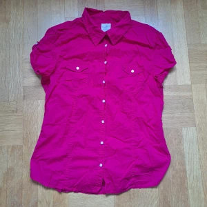 Ceriserosa kortärmad skjorta H&M L.O.G.G. - Snygg ceriserosa skjorta från H&M L.O.G.G. i storlek 46. Skjortan har korta ärmar, klassisk krage, två bröstfickor med knappar och hel knappslå framtill. 🩷