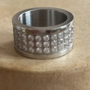 Edblad silverring med glittrande kristaller  - Snygg bred ring i silverfärgad stål  metall med flera rader av glittrande kristaller runt om. Ringen har en modern look som verkligen sticker ut. Perfekt för dig som gillar smycken.