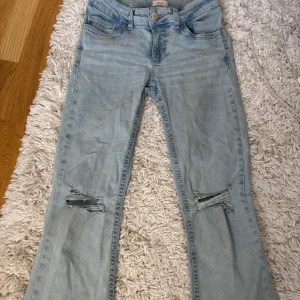 Låg midjade bootcut jeans från Nelly - Snygga ljusblå jeans från Nelly med bootcut passform och slitna detaljer vid knäna. Jeansen har inte tydliga täcken på användning, bara längs med på byxorna.Storlek :34.  Nypris: 699