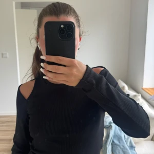 Svart ribbad topp med cut out-detaljer - Svart långärmad topp i ribbat material med trendiga cut out-detaljer på axlarna. Snygg och figurnära passform, perfekt till jeans eller kjol. Rund halsringning och stretchigt tyg som sitter skönt på kroppen. Tröjan är från Zara och i storlek S!