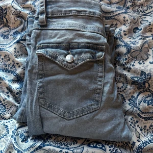 Ljusblå jeansbyxor från Gina Tricot - Säljer ett par ljusblå jeansbyxor från Gina Tricot med klassisk femficksdesign och knappdetalj på bakfickan. Byxorna har raka ben och normal passform, perfekta till vardagsstilen.