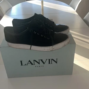 Svarta sneakers från Lanvin - Säljer ett par svarta sneakers från Lanvin med vita sulor och svarta skosnören. Skorna har en klassisk rund tå och är tillverkade i skinn. Perfekta för dig som gillar stilrena och exklusiva sneakers. Scick 7/10 då det finns tecken på användning vid cap toen hör av er vid frågor prisetr ej hugget i sten