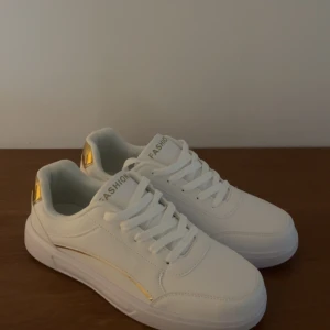 Vita sneakers med gulddetaljer - Superfina vita sneakers med gulddetaljer från SHEIN! De är helt oanvända då de inte passar. Jättebra nu inför våren och sommaren!