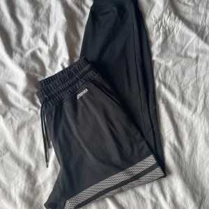 Svarta träningsbyxor från Stronger - Svarta tränings-/mjukisbyxor från Stronger med elastisk midja. Byxorna är tillverkade i mjuk polyesterblandning. Perfekta för en avslappnad stil på gymmet. Passar bra till en sport-bh. Små noppror på baksidan, märks knappt (bild 4) 🩷