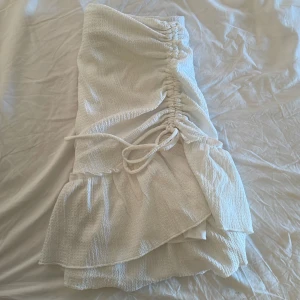 Vit omlottkjol med volang och knyt - Supersöt vit kjol med omlott-design och volangkant. Kjolen har knytband i sidan och en lätt skrynklig struktur i tyget. Perfekt för en fräsch och somrig look. Det finns ett extra vitt lager under kjolen så man ser inte igenom. Materialet är stretchigt. Skriv via frågor och mera bilder💕