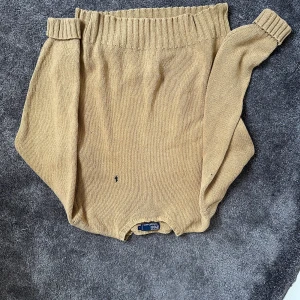 Beige stickad tröja från Polo Ralph Lauren - Säljer en klassisk beige stickad tröja från Polo Ralph Lauren. Tröjan har lång ärm, ribbade muddar och en liten broderad logga på bröstet. Perfekt för en stilren och avslappnad look.