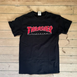 Thrasher t-shirt med röd logga - Svart t-shirt från Thrasher med den klassiska röda och vita Thrasher Magazine-loggan tryckt på bröstet. T-shirten har rund hals och korta ärmar. Litet hål under ena armen, se bild. Därav bra pris! Men enkelt att fixa med tre stygn 
