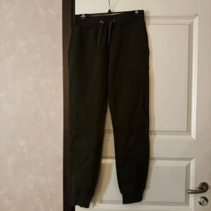 Mörkgröna mjukisbyxor med dragsko - Säljer ett par mörkgröna mjukisbyxor med resår och dragsko i midjan. Byxorna har smal passform vid anklarna och är perfekta för en avslappnad stil. Mjukt material och bekväma fickor på sidorna.