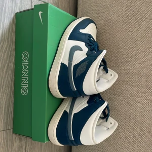 Nike Air Jordan 1 Mid blå och vita - Säljer ett par Nike Air Jordan 1 Mid i blått och vitt. Skorna har klassisk Jordan-logga på sidan och tungan, samt vit sula och blå snörning. Perfekta för dig som gillar streetwear och sneakers med retrostil.
