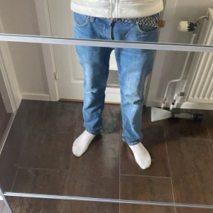 Blå jeansbyxor med normal passform - Säljer ett par klassiska blå jeansbyxor med normal passform och raka ben. Byxorna har fem fickor och stängs med dragkedja och knapp. Perfekta till vardags och passar till det mesta. Snygg och enkel design.