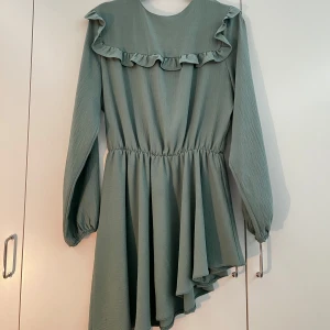 Mintgrön asymmetrisk blus  - Supersöt mintgrön blus med volang längs bröstet och långa ärmar. Klänningen har resår i midjan och ett flowy fall med asymmetrisk nederdel. Perfekt för dig som gillar en feminin och trendig stil. På tredje bilden ser man att vänsta armen har en liten skada men är ej synlig från långthåll. Storleken är 42 på plagget men är väldigt liten i storlek, pga köpt utomlands, den skulle passa bäst någon med storlek M. Priset kan diskuteras. 