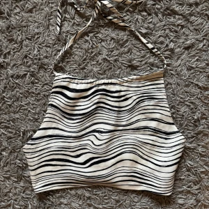Zebramönstrad croppad halterneck-top NA-KD - Säljer en croppad halterneck-top från NA-KD med svartvitt zebramönster. Toppen har knytning i nacken och smockad rygg för extra komfort. Perfekt för varma dagar och snygg att styla till jeans eller kjol🦓🤍