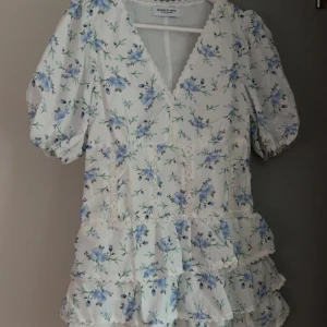 Vit blommig kortklänning med volanger - En helt ny supersöt klänning från Design By Amor, inspirerad av den trendiga Zara klänningen.  Köpte klänningen för 448 (med frakt). Men kan sälja den för 360 kr! Säljer då den inte passade mig. Storleken är S men tycker den passformen är mer som XS