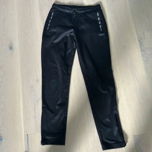 Svarta mjukisbyxor från BOSS - Svarta mjukisbyxor från BOSS med resår i midjan och dragsko. Byxorna har dragkedjeförsedda fickor med BOSS-logga på dragkedjorna. Perfekta för en avslappnad stil och bekväma att bära hela dagen.