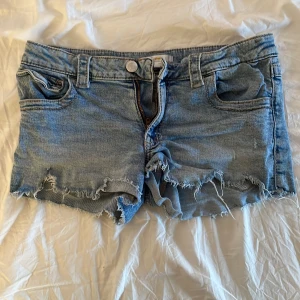 Ljusblå jeansshorts med fransar från Gina Tricot - Ljusblå jeansshorts med råa fransade kanter och klassisk femficksdesign. Shorts med knapp och dragkedja framtill samt bälteshällor. Bakfickor med lock och knapp. Perfekta för sommaren! Skicka om frågar och om ni undrar hur som sitter på💕