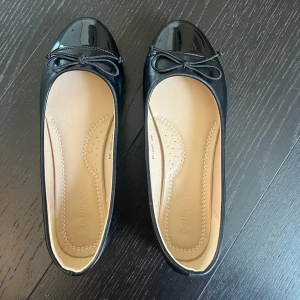 Svarta ballerinaskor med rosett från Bellucci - Säljer ett par klassiska svarta ballerinaskor från Bellucci med glansig tå och söt rosettdetalj framtill. Skorna har rund tå och platt sula. Använda 1 gång bara då dom tyvärr var för små för mig.
