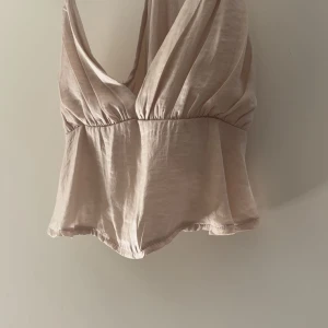 Beige omlottopp med djup v-ringning - Säljer en beige omlottopp med djup v-ringning och tunna axelband. Jätte skönt material