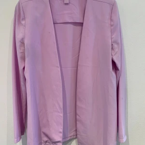 Ljuslila kavaj från Object - Säljer en stilren ljuslila kavaj från Object. Jackan har öppen front utan knäppning och långa ärmar. Perfekt för dig som vill addera lite färg till din outfit. Enkel och rak passform.