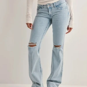 Ljusblå bootcut jeans med slitningar - Säljer ett par ljusblå bootcut jeans med slitna hål över knäna och broderade detaljer på bakfickorna. Köpt för 699, säljer nu för använder dom sällan