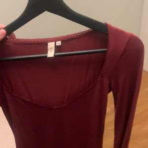 Vinröd långärmad topp från nelly - Vinröd långärmad topp från Nelly med v-ringning och dekorativ spetskant vid halsen. Tunn och mjuk i materialet, perfekt att styla till olika outfits.