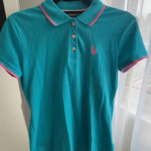 U.S. Polo Assn. Piketröja  - Turkos pikétröja från U.S. Polo Assn. med rosa detaljer på krage och ärmslut samt broderad logga på bröstet. Klassisk piké med knappslå och korta ärmar. Tillverkad i bomull och lite spandex för stretch. Likadan som min lila också (finns i min bio) och köptes i USA för 800kr. 