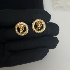 Guldiga örhängen med LV-logga - Säljer ett par runda guldiga örhängen med LV-logga i mitten. Örhängena är dekorerade med små glittrande stenar runt kanten för en lyxig känsla. Perfekt accessoar för att lyfta din stil.