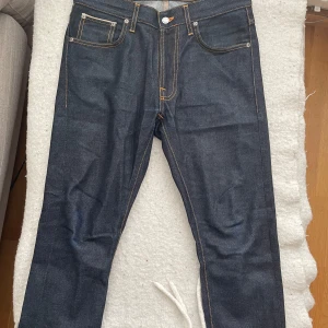 Mörkblå jeans från Nudie Jeans - Säljer ett par mörkblå jeans från Nudie Jeans med klassisk femficksdesign och kontrastsömmar. Jeansen har raka ben och normal passform. Riktigt fint skick. Storlek 30/30