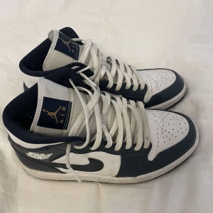 Nike Air Jordans  - Säljer ett par Nike Air Jordans i vitt och marinblått med klassisk hög modell. Bra skick, endast märkvärdigt är att de är lätt creasade.