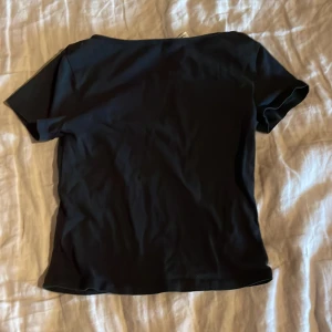 Svart croppad topp från Gina Tricot - En enkel svart croppad topp från Gina Tricot med rund, djup urringning och korta ärmar. Perfekt att matcha med jeans eller kjol för en stilren look.