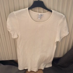 Vit ribbad t-shirt från & Other Stories - Säljer en enkel och stilren vit ribbad t-shirt från & Other Stories, Stockholm Atelier. T-shirten har rund halsringning och korta ärmar. Perfekt basplagg i mjuk bomullskvalitet.