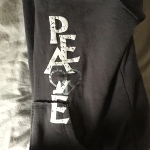Mörkgrå hoodie med tryck från Cocoa Platinum - Mysig mörkgrå hoodie med vit teddyfoder på insidan och stort tryck med texten 'PEACE' i vitt och silver på ena ärmen. Jackan har huva och två fickor framtill. Perfekt för kyliga dagar. Den är använd men inte sliten den är väldig mysig och varm och passar mycket till jeans