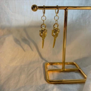 Silver eller guldärgade örhängen med fågelkranium - Unika örhängen i silver eller guld färg med detaljerade hängen formade som fågelkranium. Perfekta för dig som gillar annorlunda och edgy smycken. Säljs som par och passar till många olika stilar.