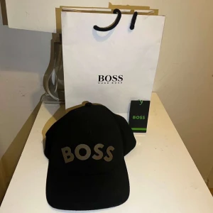 Svart keps från Hugo Boss - Snygg svart keps från Hugo Boss med stor BOSS-logga framtill. Klassisk böjd skärm och justerbar passform. Perfekt accessoar för en stilren look.
