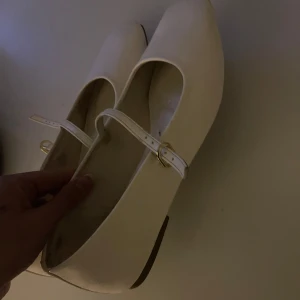 Vita ballerinaskor med rem - Säljer ett par vita ballerinaskor med smal rem över foten och rund tå. Små skavanker som syns på bild