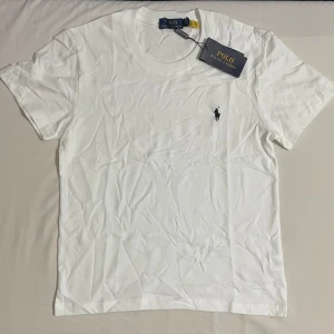 Vit t-shirt från Polo Ralph Lauren - Klassisk vit t-shirt från Polo Ralph Lauren med rund halsringning och den ikoniska broderade loggan på bröstet. Perfekt basplagg i mjuk bomull som passar till allt.