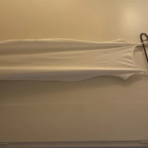 Vit tight klänning med smala axelband - Enkel och stilren vit klänning med smala axelband och tight passform. Klänningen är ärmlös och har en rak, kroppsnära siluett som passar perfekt till sommaren. Materialet känns mjukt och stretchigt.